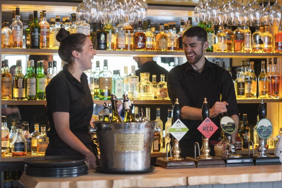 Two members of staff standing behind the bar laughing with each other